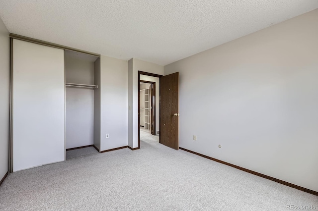 unfurnished bedroom featuring baseboards, light carpet, a closet, and a textured ceiling