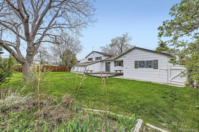 rear view of house featuring fence, a shingled roof, and a lawn