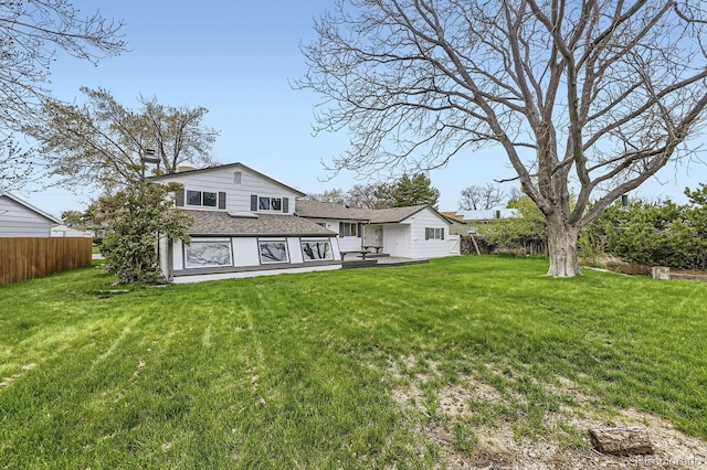 back of property with a chimney, roof with shingles, fence, and a lawn