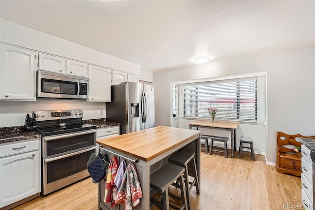 kitchen featuring light wood-style flooring, appliances with stainless steel finishes, white cabinetry, and wooden counters