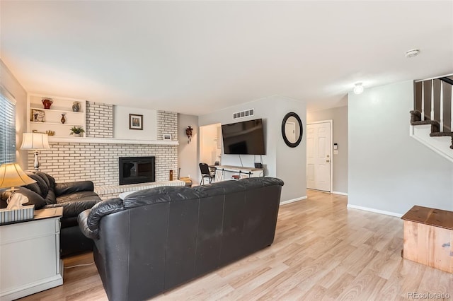 living room featuring a fireplace, light wood-style floors, baseboards, visible vents, and stairway