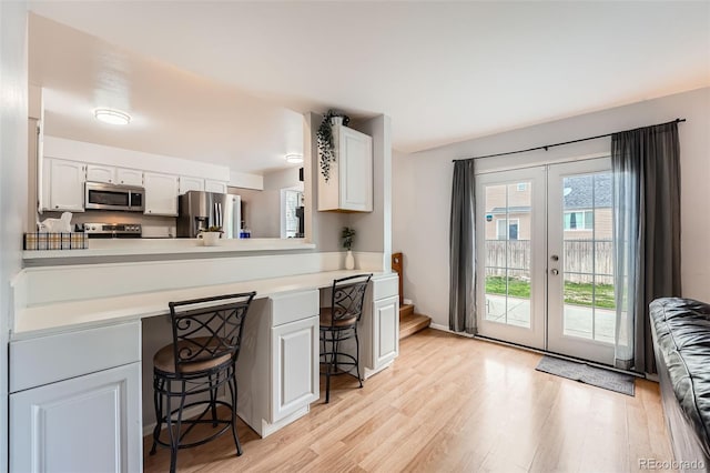 kitchen with a breakfast bar area, french doors, appliances with stainless steel finishes, light countertops, and light wood-style floors
