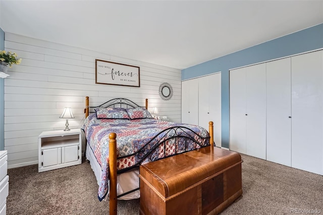 carpeted bedroom with wood walls and two closets