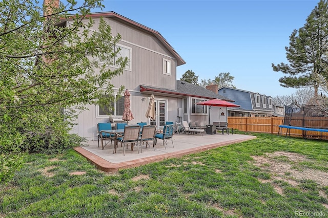 back of house featuring a chimney, a trampoline, fence, a yard, and a patio