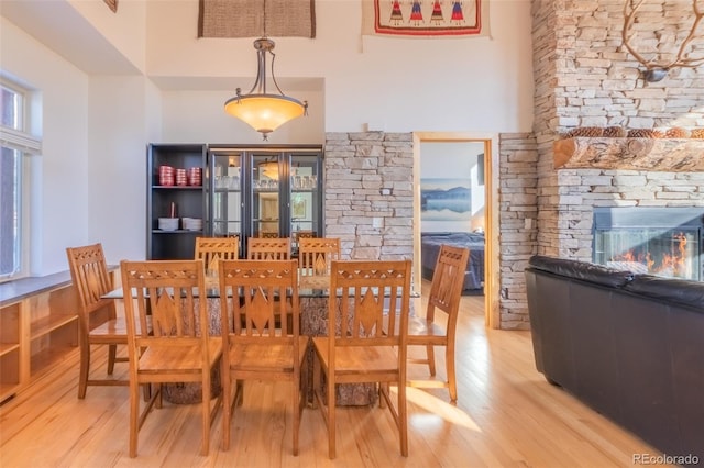 dining space featuring light hardwood / wood-style floors, a towering ceiling, and a fireplace