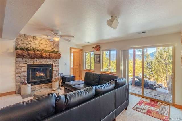 carpeted living room featuring ceiling fan, a stone fireplace, and a textured ceiling