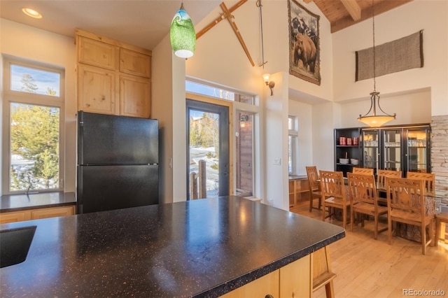 kitchen with light brown cabinets, black fridge, hanging light fixtures, and a wealth of natural light