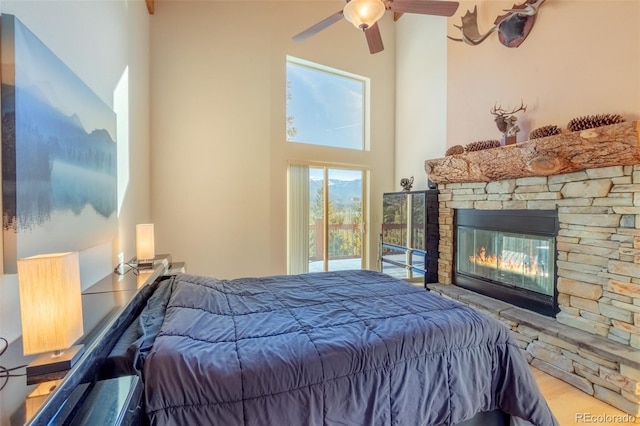 bedroom with ceiling fan, a towering ceiling, a stone fireplace, and light wood-type flooring