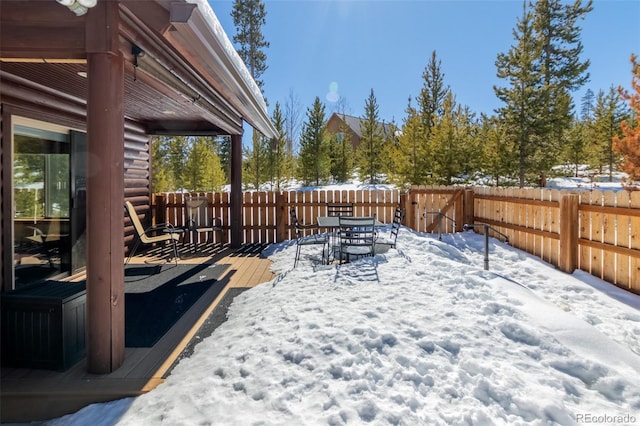 yard covered in snow with a deck, outdoor dining space, and a fenced backyard