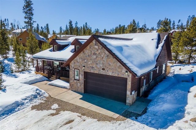 view of snowy exterior with stone siding and an attached garage