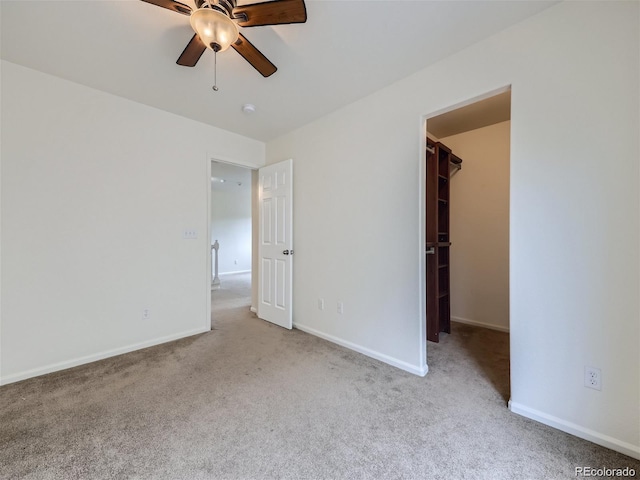 unfurnished bedroom featuring a spacious closet, a closet, ceiling fan, and light colored carpet