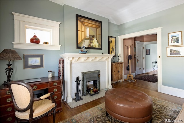 living area featuring a fireplace with flush hearth, baseboards, and wood finished floors