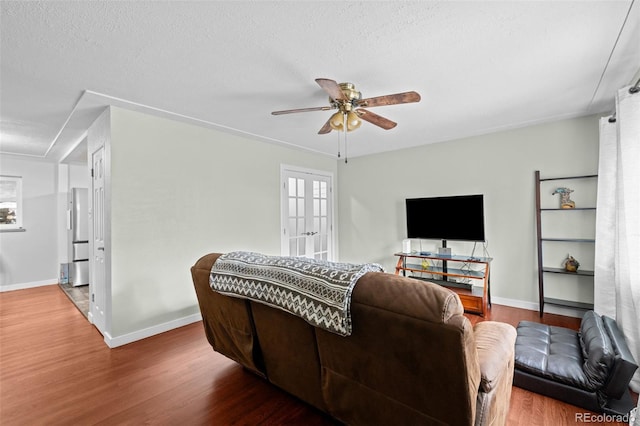 living room with french doors, a ceiling fan, a textured ceiling, wood finished floors, and baseboards