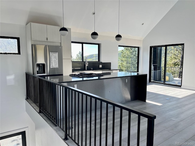 kitchen with pendant lighting, light hardwood / wood-style flooring, stainless steel fridge, high vaulted ceiling, and decorative backsplash