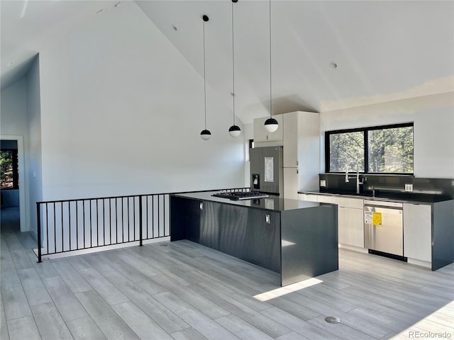 kitchen with light hardwood / wood-style floors, appliances with stainless steel finishes, white cabinetry, decorative light fixtures, and high vaulted ceiling