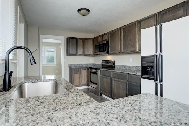 kitchen featuring a textured ceiling, appliances with stainless steel finishes, dark brown cabinets, light stone counters, and sink