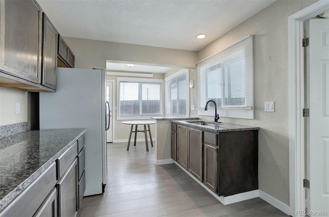 kitchen featuring a textured ceiling, white refrigerator, dark brown cabinets, wood-type flooring, and sink