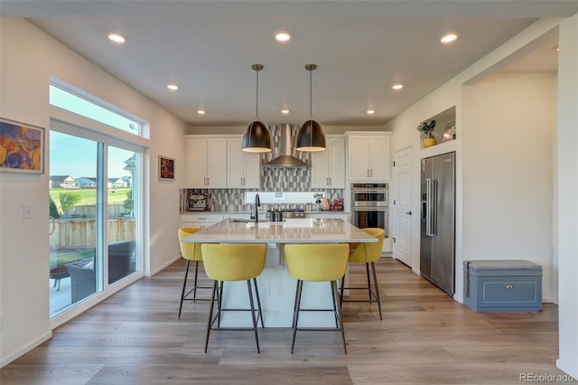 kitchen featuring a kitchen island with sink, tasteful backsplash, decorative light fixtures, white cabinetry, and stainless steel appliances