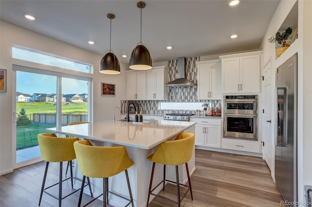 kitchen with appliances with stainless steel finishes, decorative light fixtures, white cabinetry, and wall chimney exhaust hood