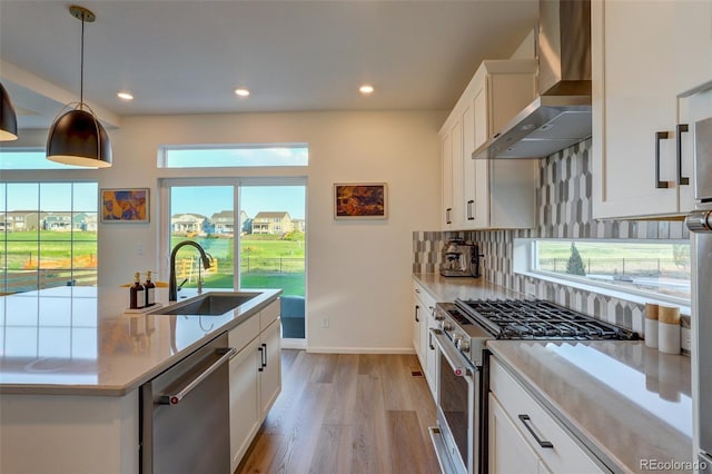 kitchen featuring wall chimney range hood, hanging light fixtures, sink, appliances with stainless steel finishes, and white cabinetry