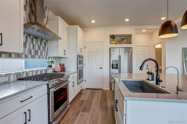 kitchen featuring appliances with stainless steel finishes, sink, wall chimney range hood, white cabinetry, and hanging light fixtures