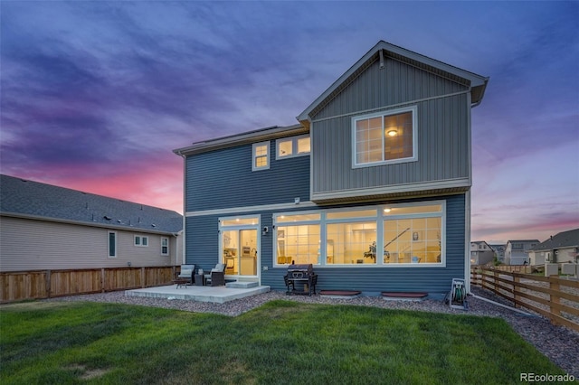 back house at dusk featuring a yard and a patio