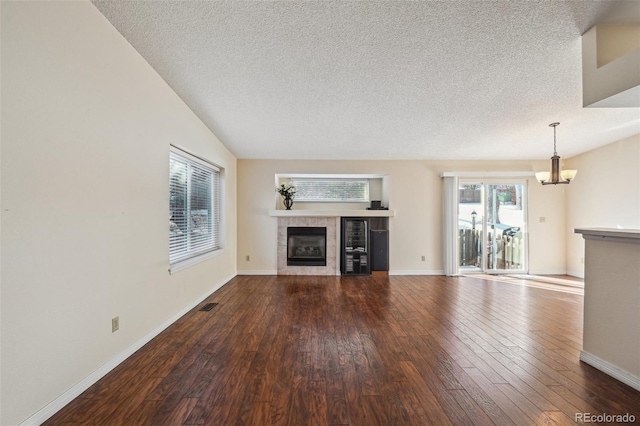 unfurnished living room featuring lofted ceiling, a tile fireplace, an inviting chandelier, wood-type flooring, and a textured ceiling