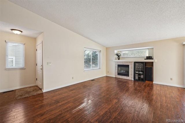 unfurnished living room featuring a tile fireplace, vaulted ceiling, wood-type flooring, and a textured ceiling