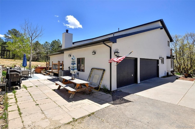 1673 Woodmoor Dr, Monument, CO 80132 - back of house with stucco siding, a chimney, concrete driveway, and a patio area