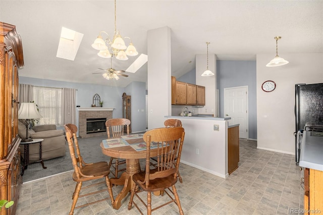 dining room with lofted ceiling with skylight, a fireplace, baseboards, and ceiling fan