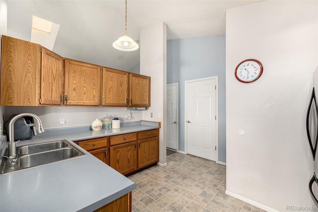 kitchen featuring baseboards, decorative light fixtures, light countertops, brown cabinetry, and a sink