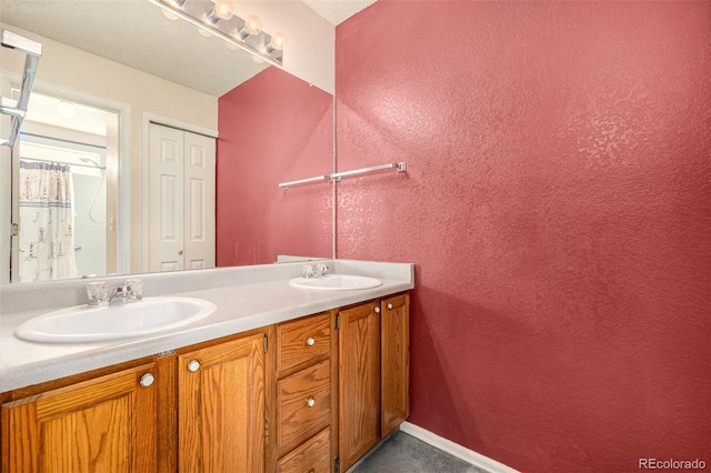 full bathroom featuring a sink, baseboards, double vanity, and a textured wall