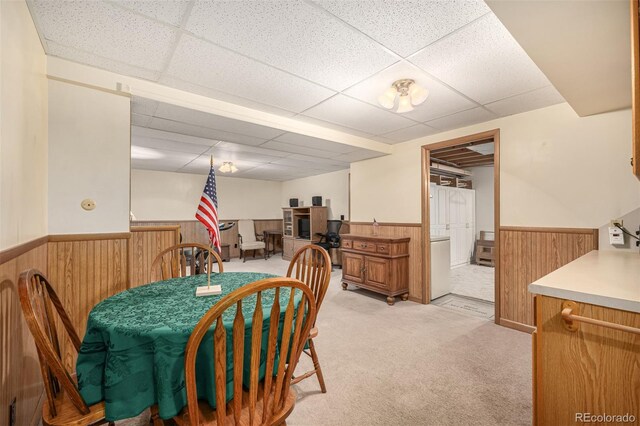 dining area with wooden walls, light colored carpet, a drop ceiling, and wainscoting