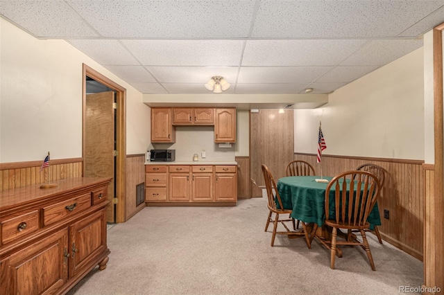 dining area featuring a paneled ceiling, light carpet, wooden walls, and wainscoting