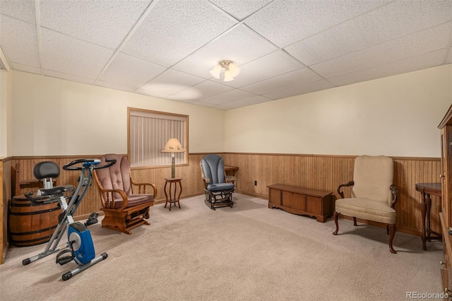 living area with carpet flooring, a paneled ceiling, wood walls, and wainscoting