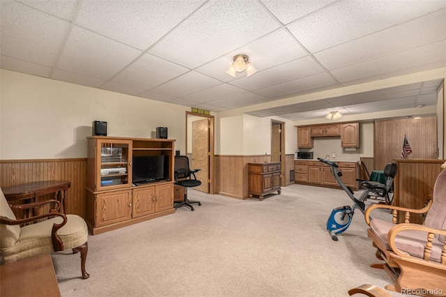 interior space with a wainscoted wall, light carpet, bar, wood walls, and a paneled ceiling