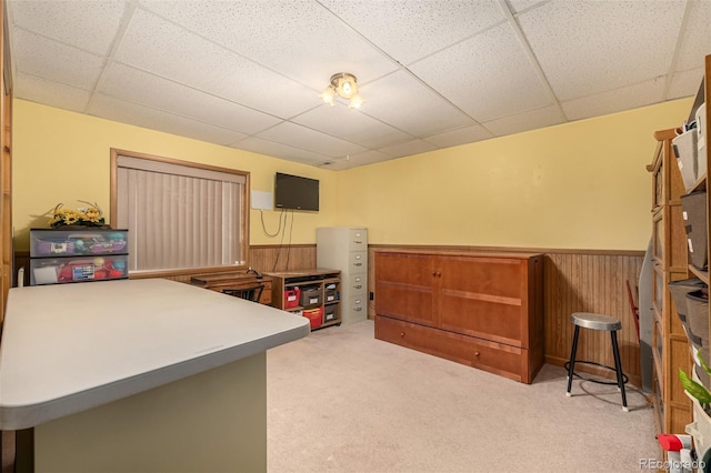 interior space featuring light colored carpet, a drop ceiling, wooden walls, and wainscoting