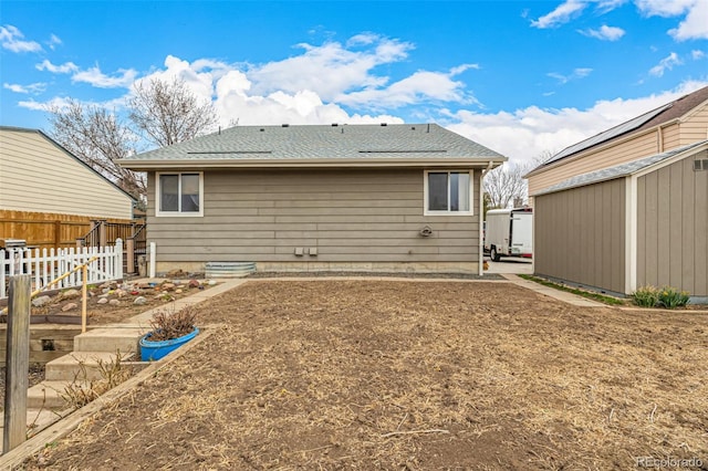 rear view of property with fence, a patio area, roof with shingles, a storage shed, and an outbuilding