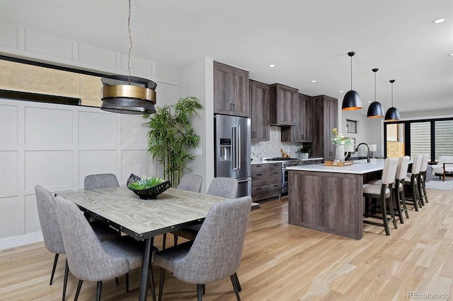 kitchen with dark brown cabinetry, hanging light fixtures, light hardwood / wood-style flooring, high quality appliances, and a kitchen island with sink