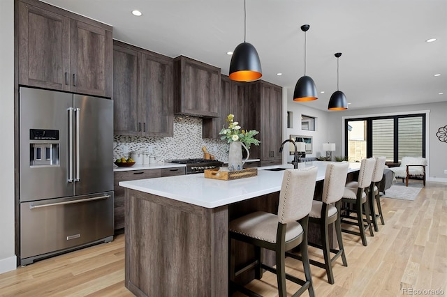 kitchen with appliances with stainless steel finishes, light wood-type flooring, dark brown cabinets, and an island with sink