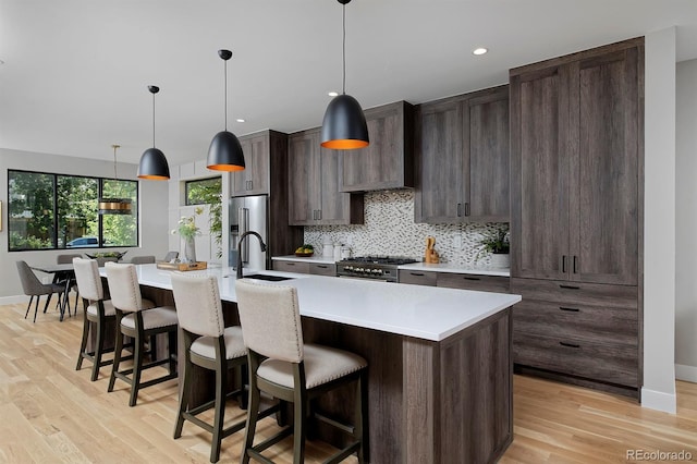 kitchen featuring sink, a kitchen island with sink, hanging light fixtures, high quality appliances, and light wood-type flooring