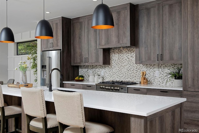 kitchen featuring decorative backsplash, hanging light fixtures, a kitchen island with sink, and appliances with stainless steel finishes