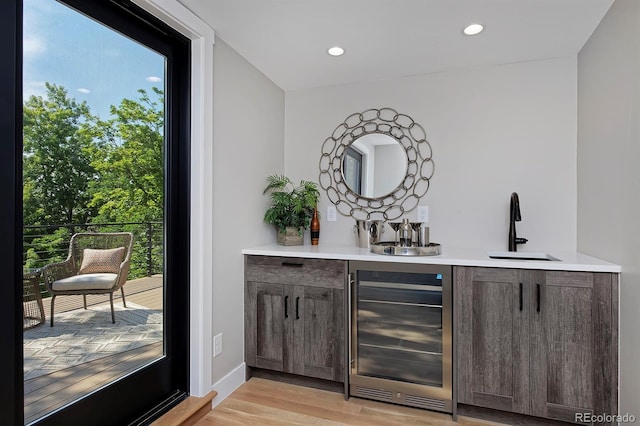 bar with sink, dark brown cabinets, beverage cooler, and light hardwood / wood-style flooring