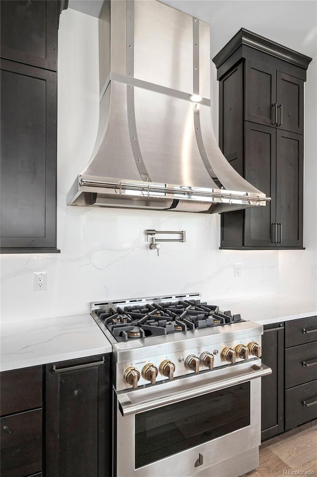 kitchen with wall chimney range hood, light stone countertops, high end stainless steel range oven, and light hardwood / wood-style floors