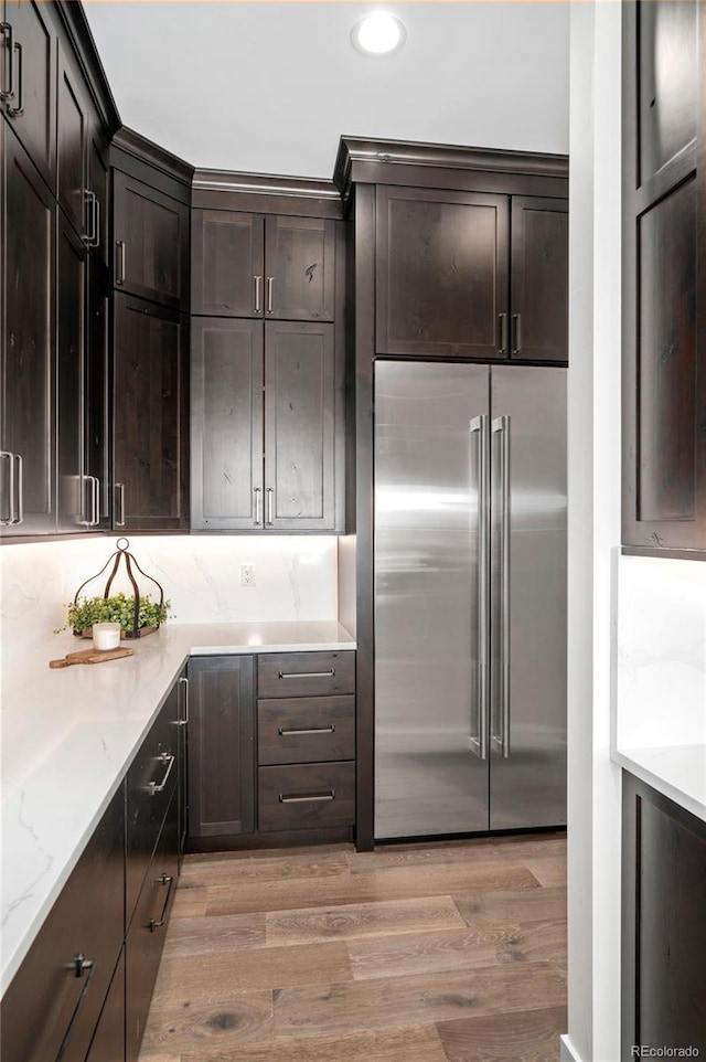 kitchen featuring light stone counters, dark brown cabinetry, light hardwood / wood-style flooring, and built in refrigerator