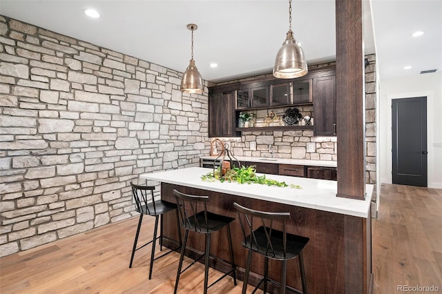 bar with sink, light hardwood / wood-style flooring, hanging light fixtures, and dark brown cabinets