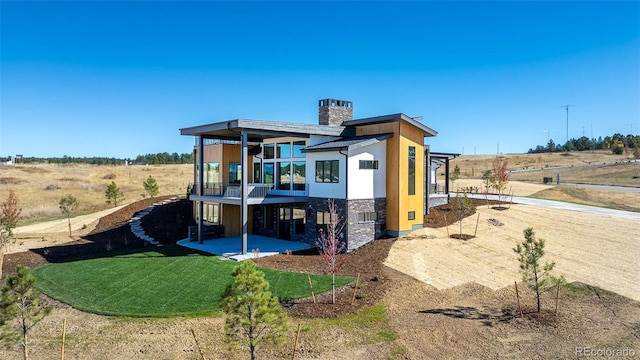 back of property featuring a balcony, a lawn, and a rural view