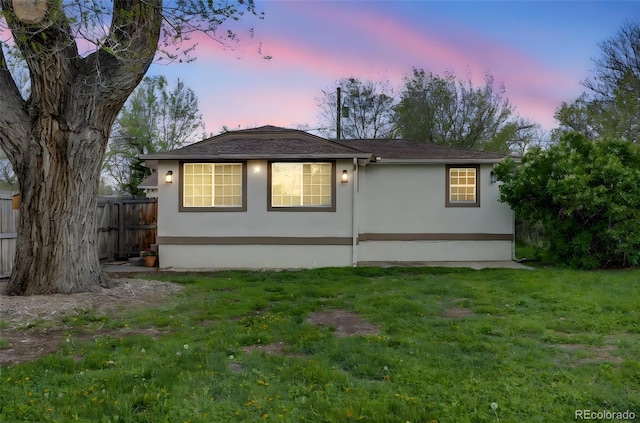 rear view of house with fence, stucco siding, and a yard