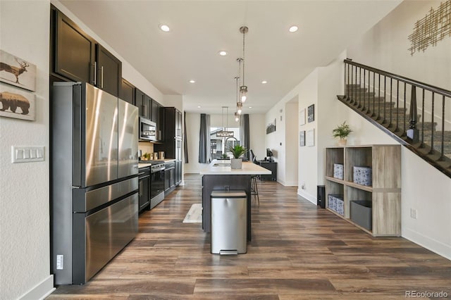 kitchen featuring appliances with stainless steel finishes, light countertops, dark wood-type flooring, and an island with sink