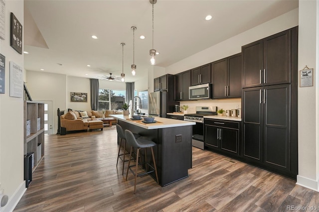 kitchen with stainless steel appliances, dark wood-type flooring, light countertops, a kitchen bar, and a center island with sink